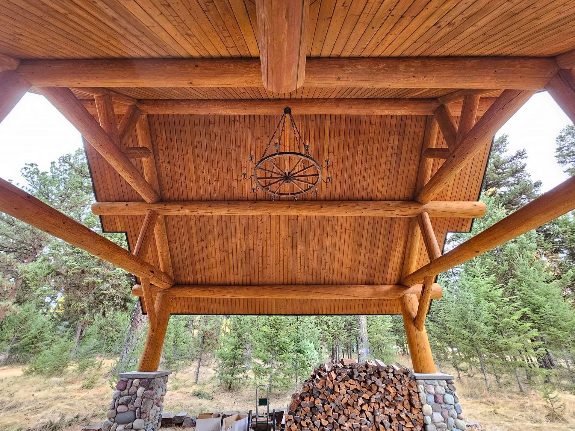 Wooden outdoor structure with stone pillars, a stacked firewood pile, and a decorative ceiling light.