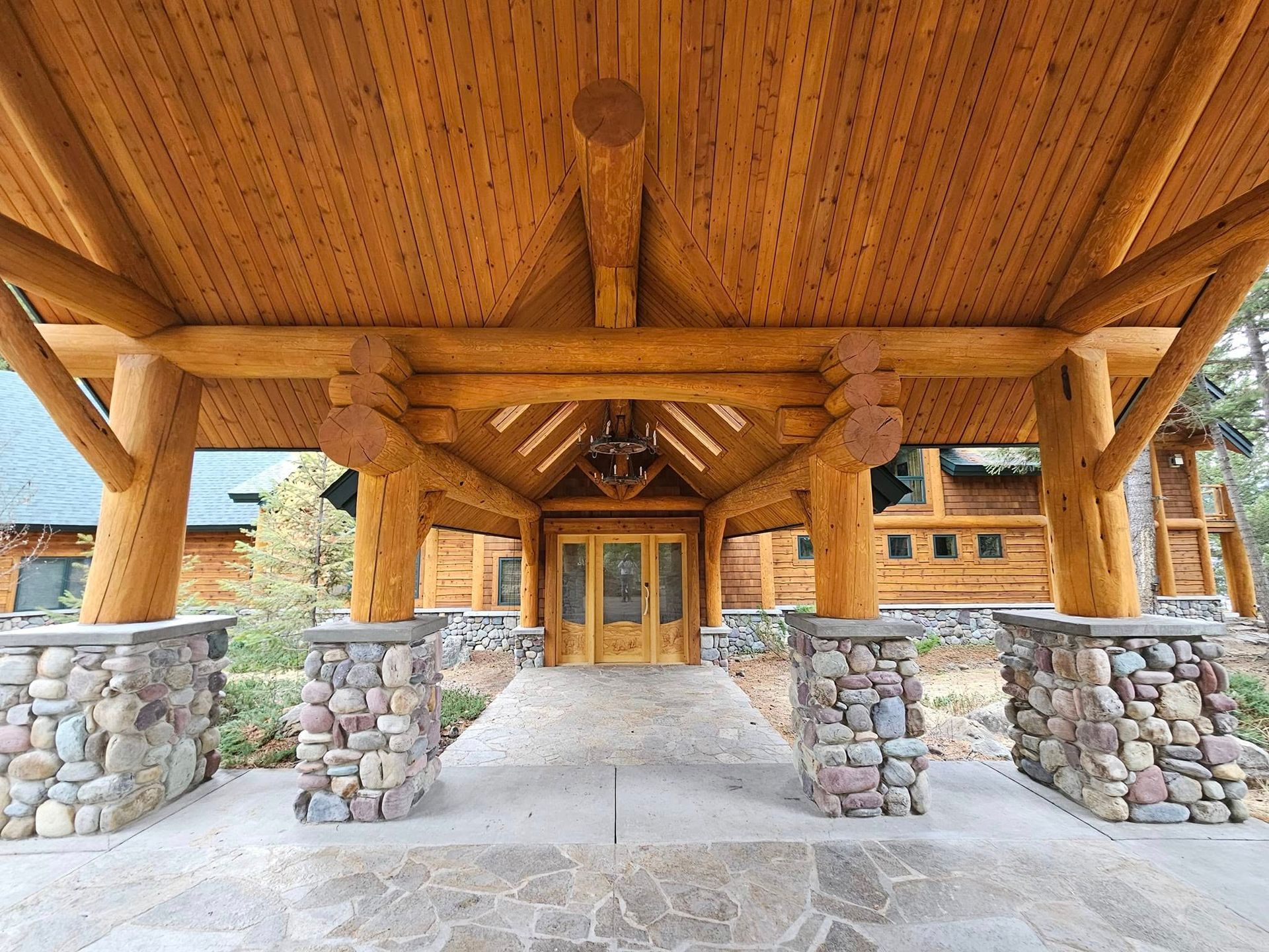 Wooden lodge entrance with stone pillars, log beams, and a wood door.