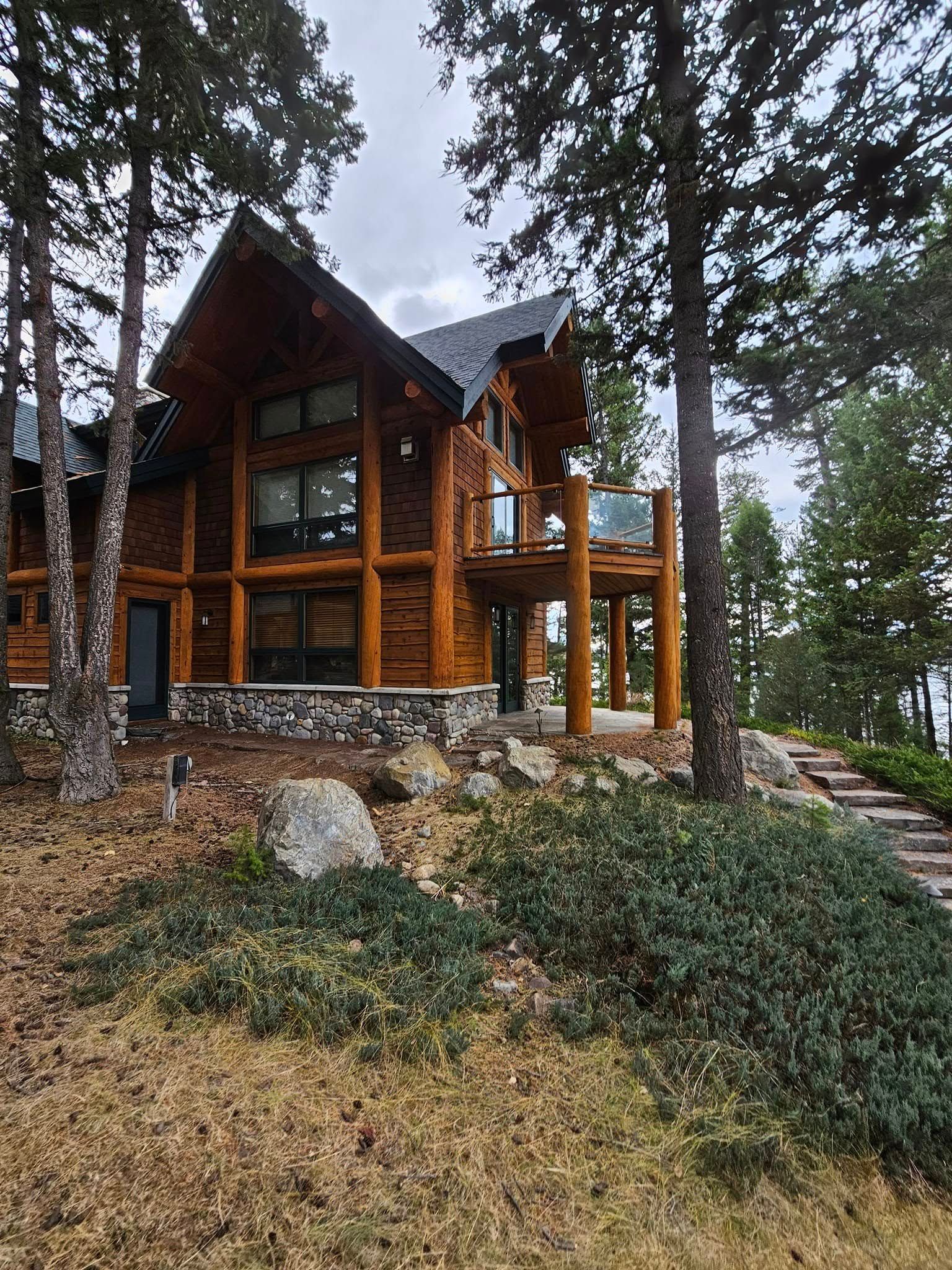 Log cabin home with a deck, surrounded by trees and greenery.