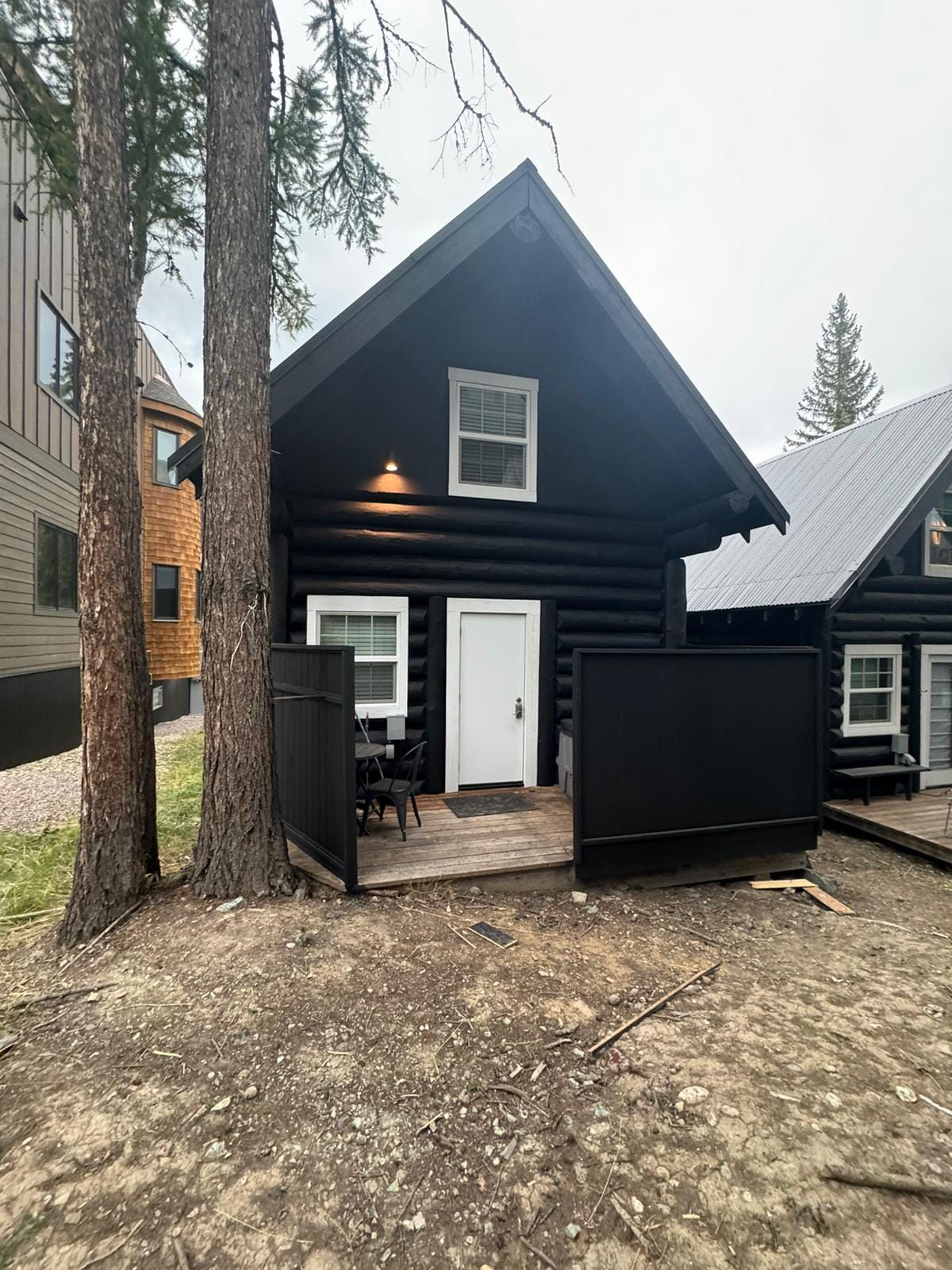 Black cabin with white door and window, small porch. Trees frame the front.