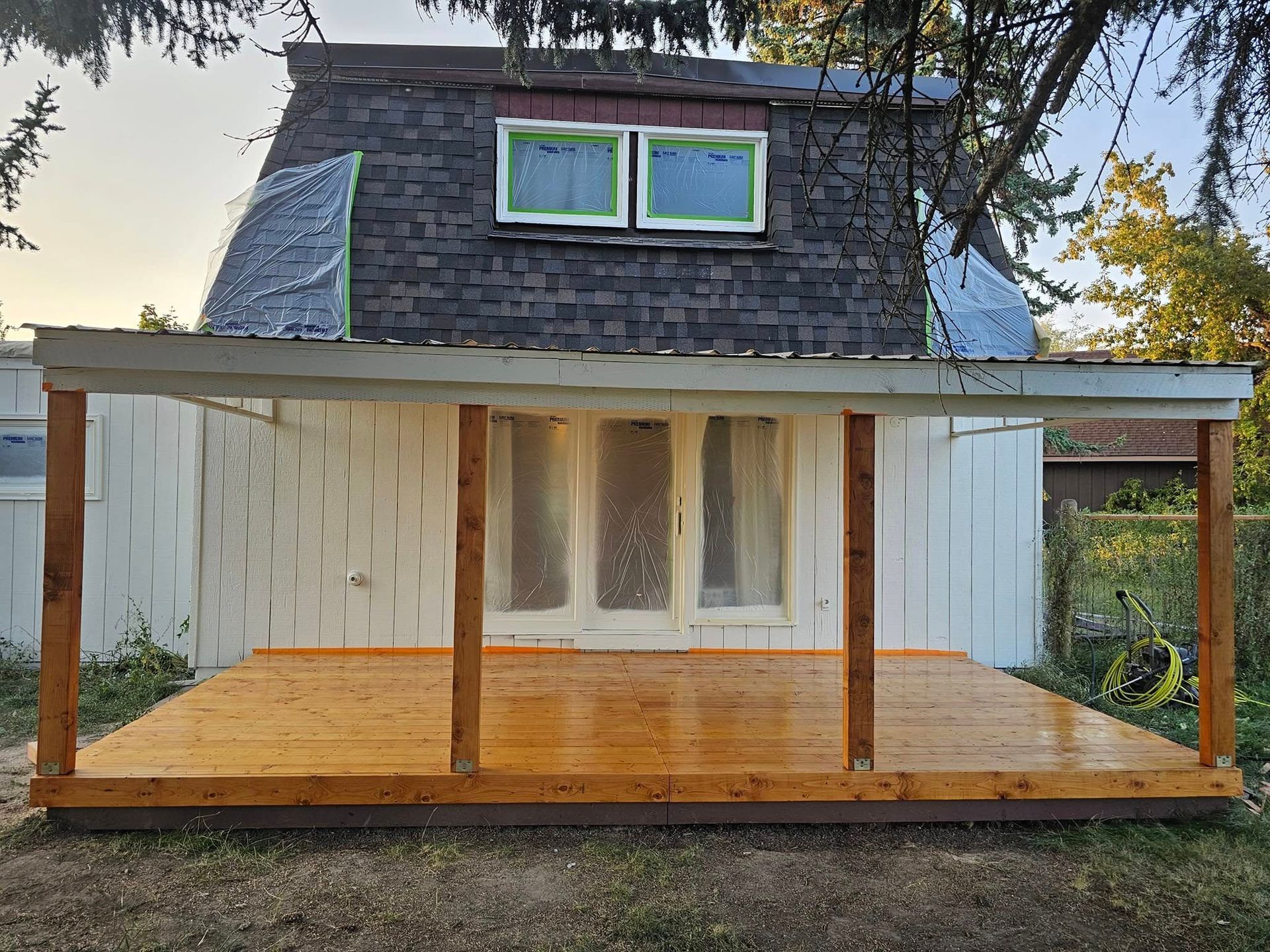 Backyard deck with wooden posts and canopy; white house with dark roof in the background.