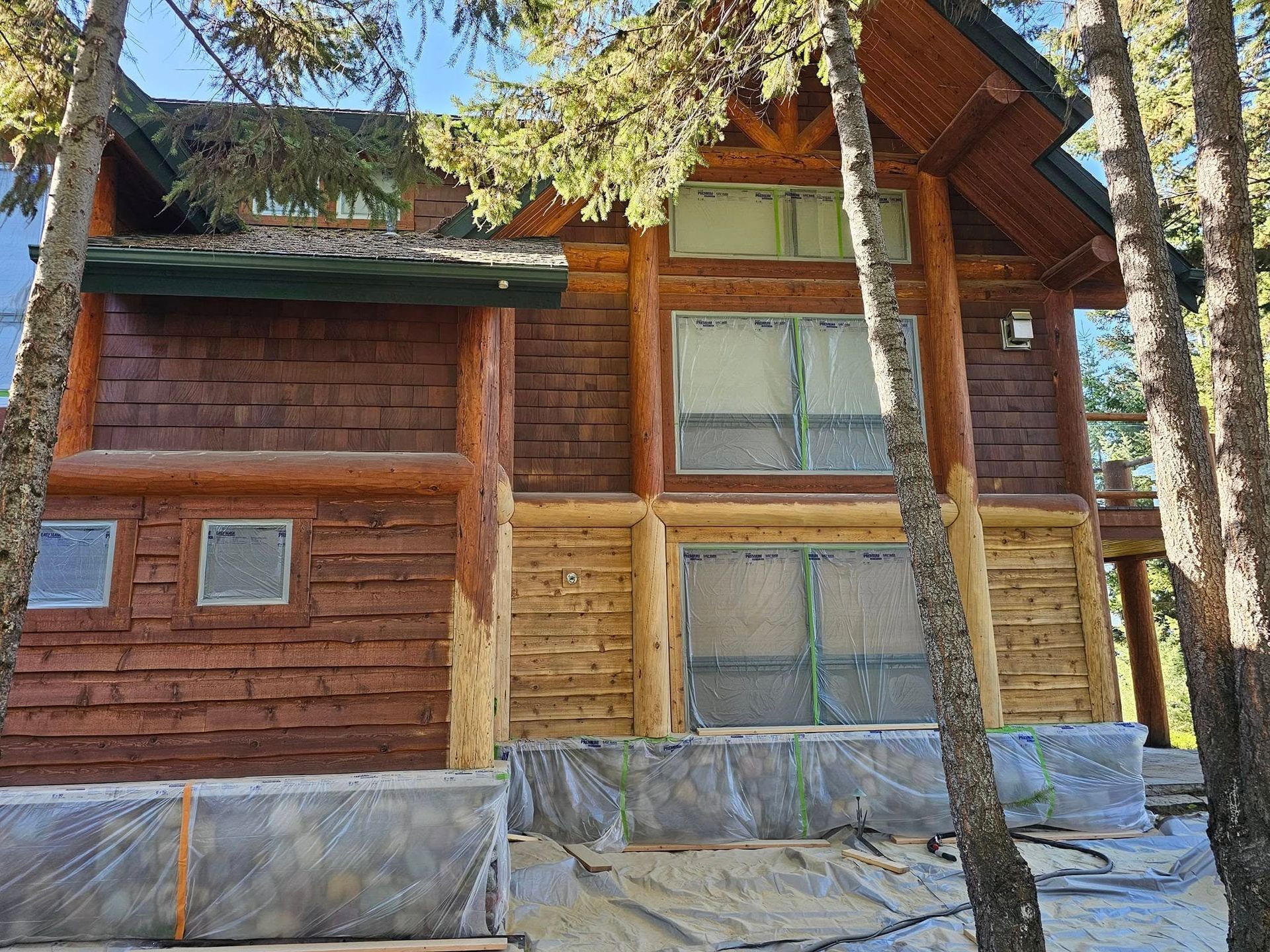 Log cabin exterior with varying shades of brown wood, surrounded by trees and covered windows.