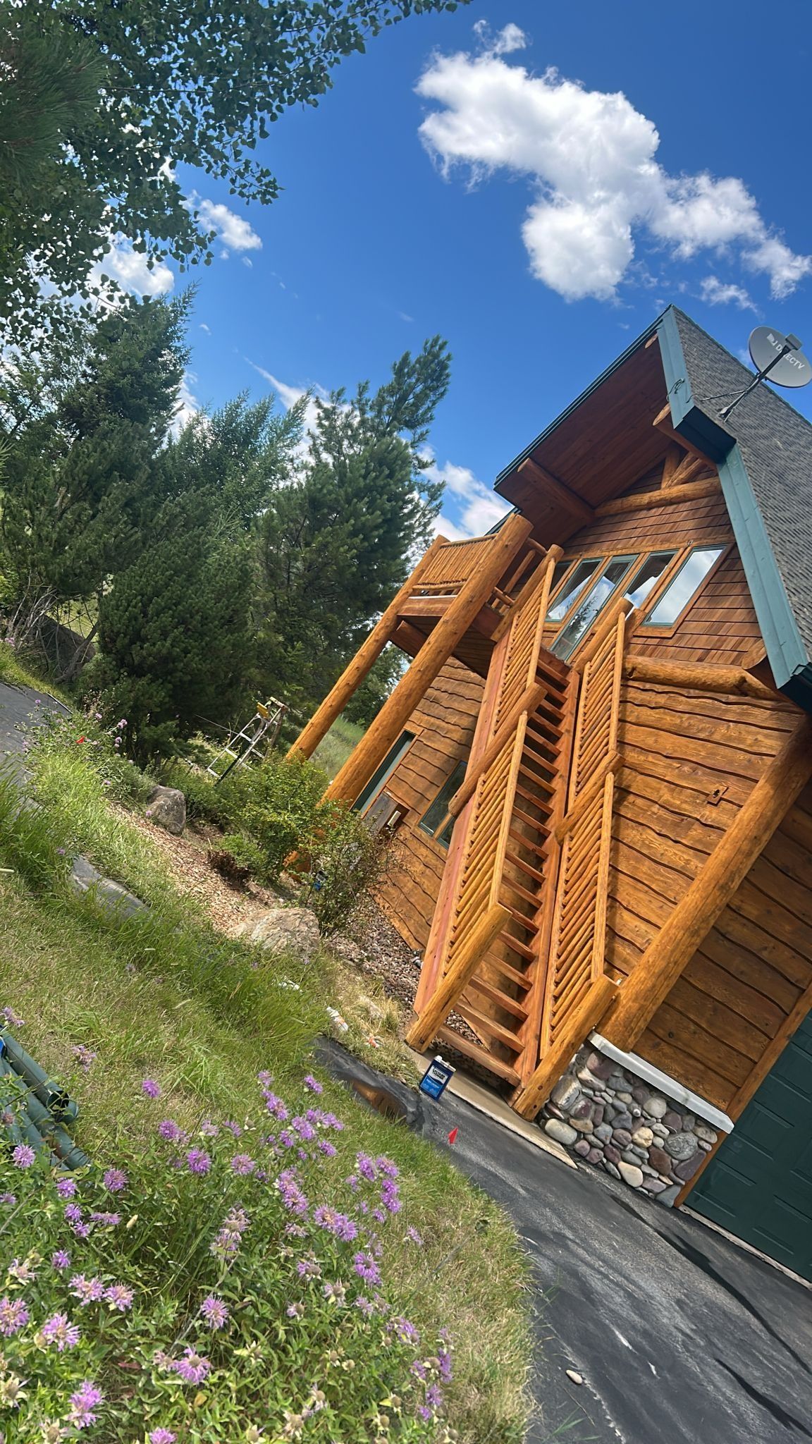 Wooden cabin with a staircase on a hillside under a blue sky.