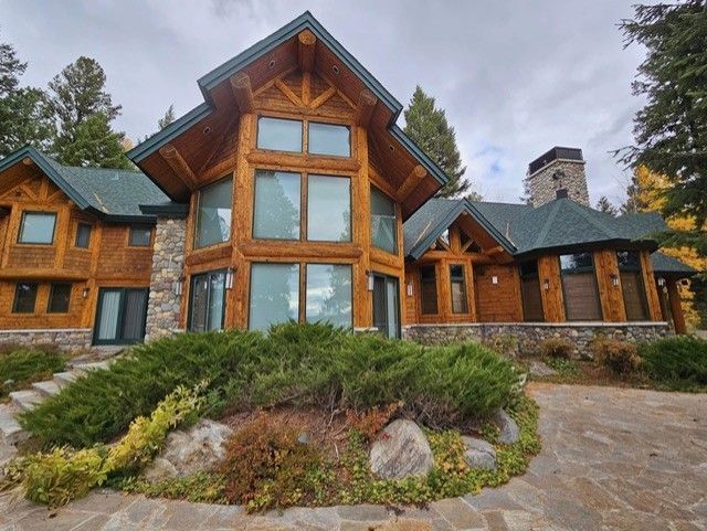Log cabin home with large windows, stone accents, and manicured landscaping under a cloudy sky.