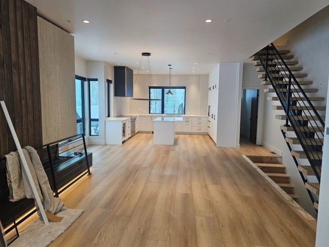 Modern home interior with light wood floors, kitchen with white cabinets, and a staircase.