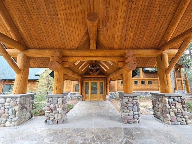 Log cabin entrance with stone columns supporting a wooden roof.