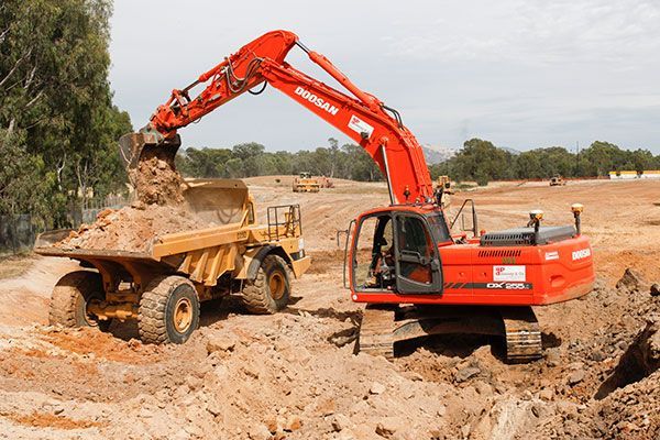 A red excavator is loading dirt into a dump truck.
