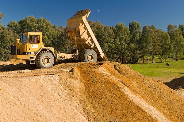 A yellow dump truck is driving over a pile of dirt.