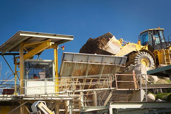 A yellow bulldozer is loading rocks into a dumpster at a construction site.