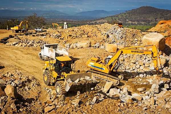 A large yellow excavator is moving rocks in a quarry.
