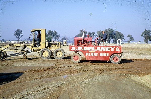 A man is driving a red truck that says a.p. delaney plant hire on it.