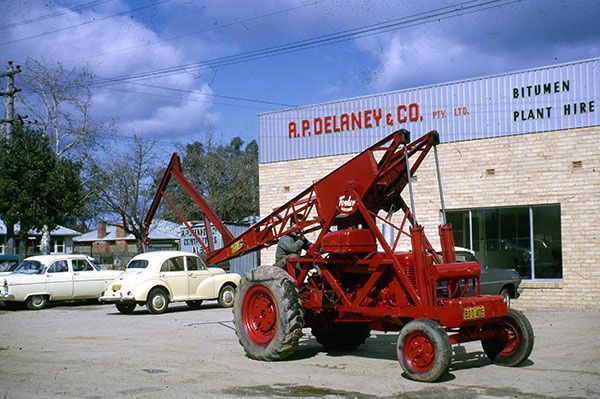 A red tractor is parked in front of a building that says bitumen plant hire
