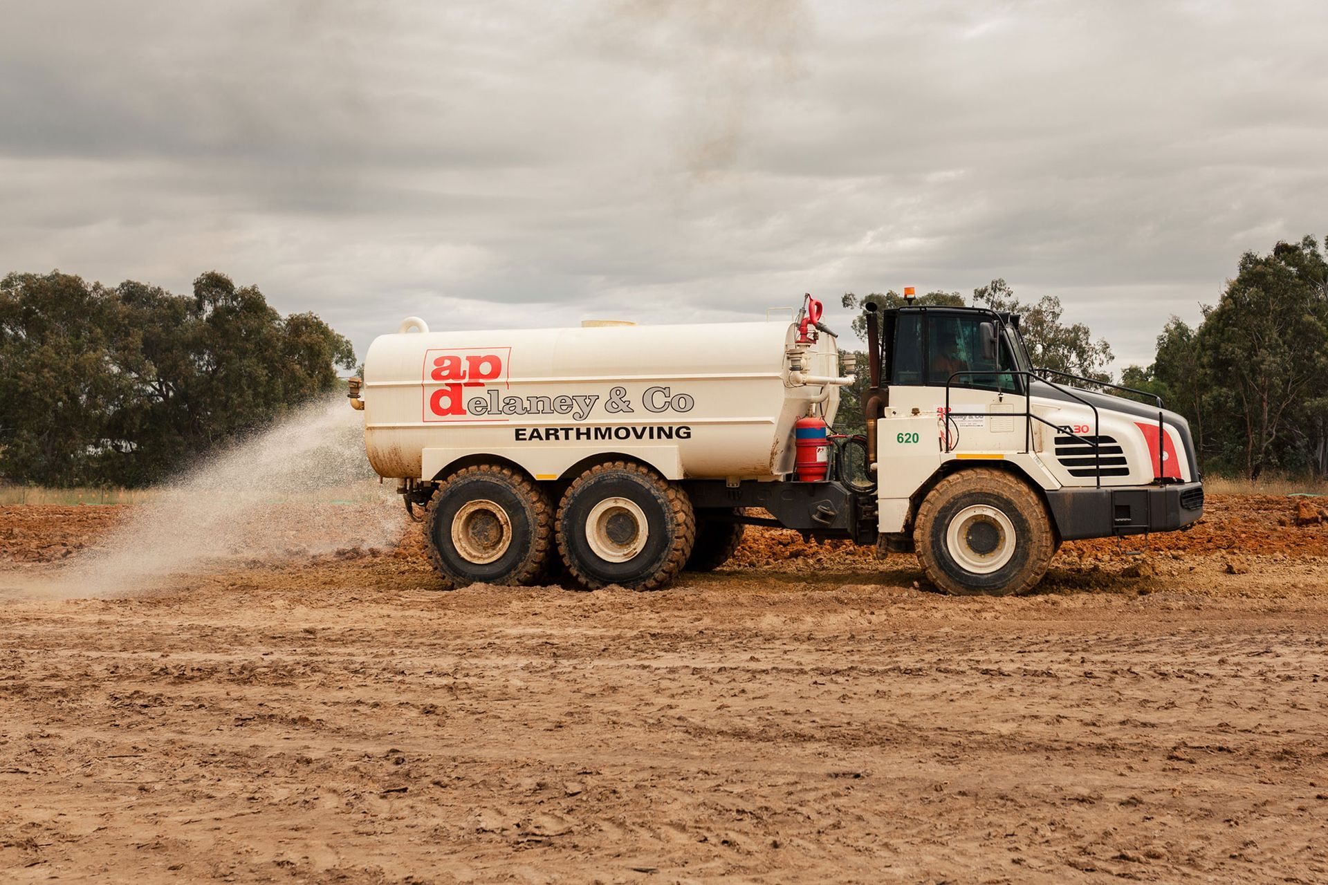 A white truck is spraying water on a dirt field.