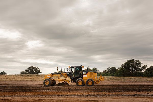 A yellow tractor is driving through a dirt field on a cloudy day.