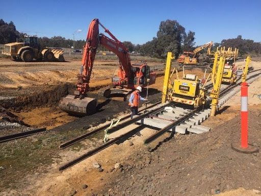 A man is standing on a train track next to a bulldozer.