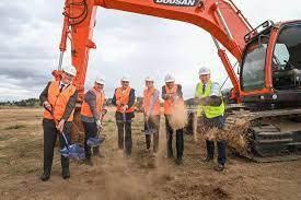A group of construction workers are shoveling dirt in front of an excavator.