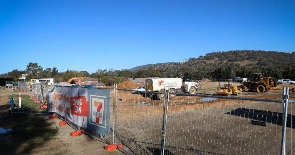 A construction site with a fence and tractors in the background.