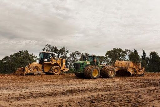 A group of construction vehicles are parked in a dirt field.