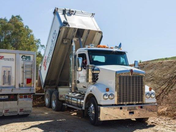 A dump truck is driving down a dirt road next to a trailer.