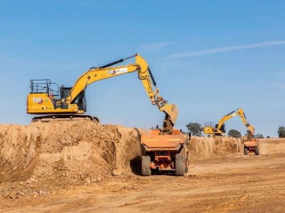 A yellow excavator is loading dirt into a dump truck.