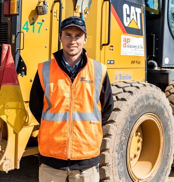 A man in an orange vest is standing in front of a cat tractor