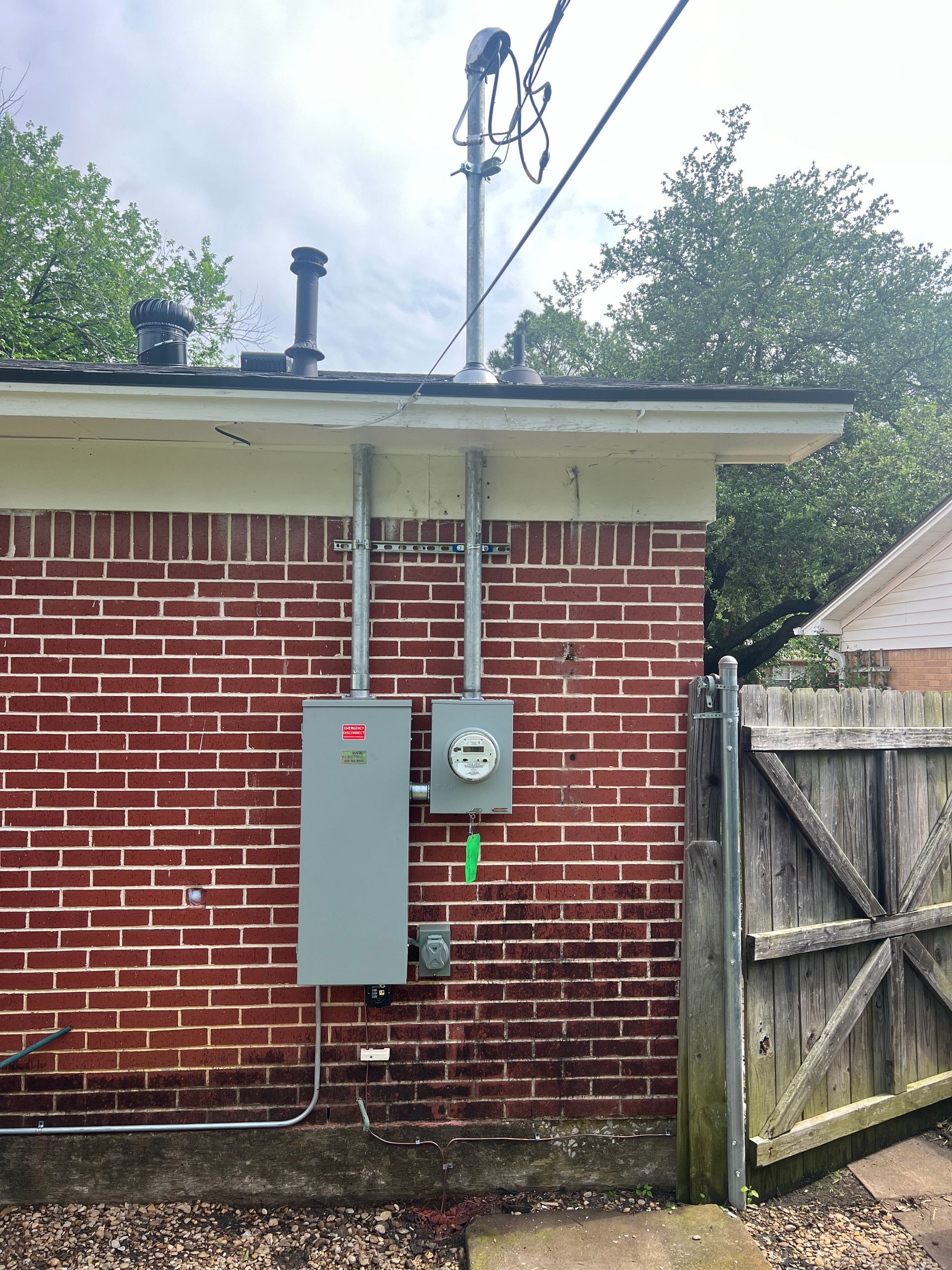 Brick house exterior with gray utility panels, power lines, and a wooden gate by the side yard