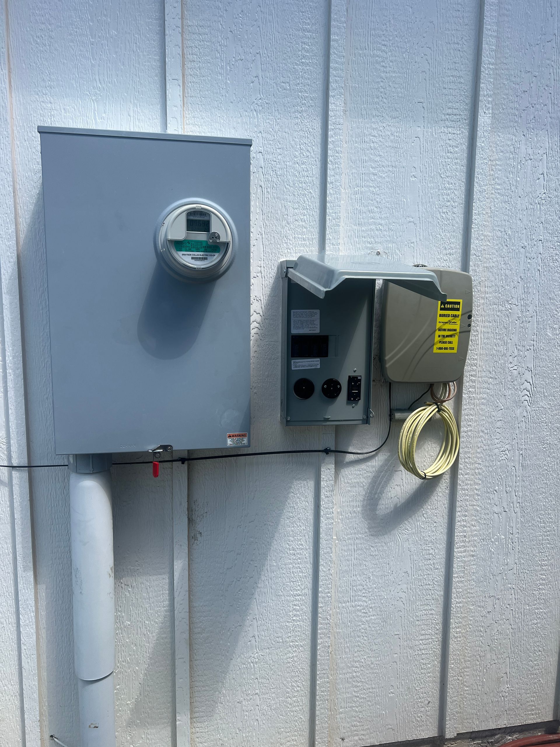 Electric meter and utility boxes mounted on a gray exterior wall.