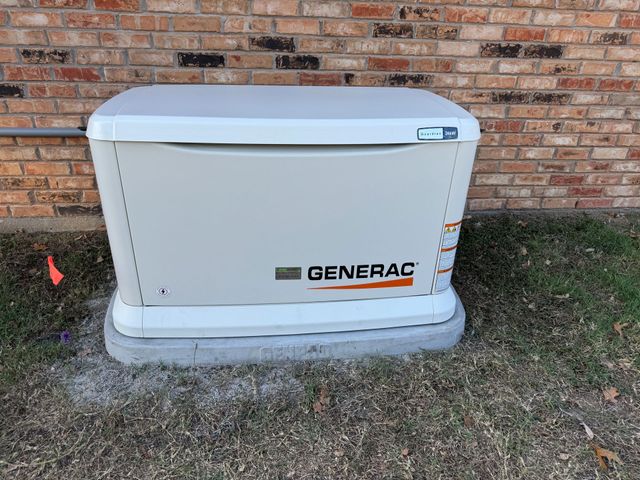 White Generac home backup generator beside a brick wall on a concrete pad