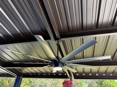 Ceiling fan mounted under a corrugated metal roof with exposed beams.
