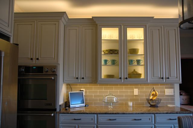 Modern kitchen with cream cabinets, glass-front uppers, tile backsplash, and built-in oven.