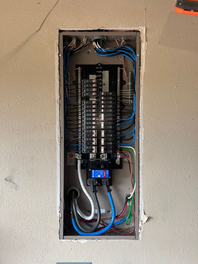 Open electrical breaker panel with tangled blue and black wires in a wall recess