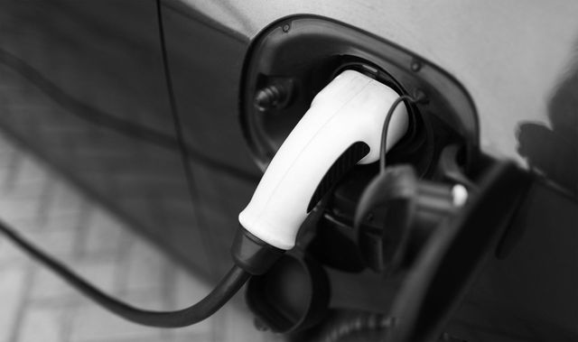 Electric vehicle charging plug connected to a car charge port, close-up in black and white