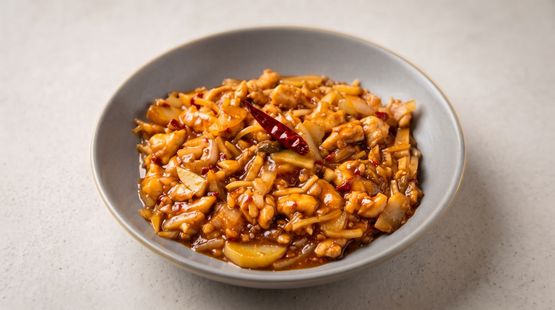 A bowl of spicy saucy pasta or stir-fry with red chili on a gray surface.
