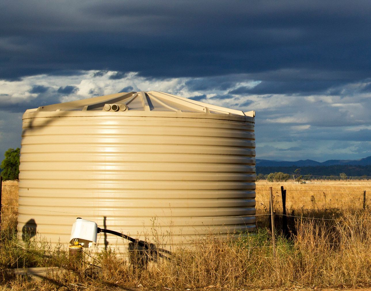 Large tan water tank in a field under a cloudy, dramatic sky. Large tan water tank in a field under a cloudy, dramatic sky.