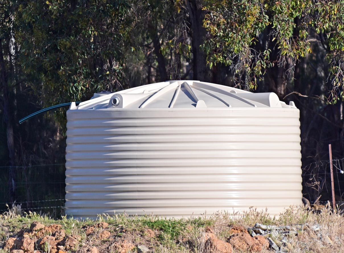 Tan corrugated water tank in a grassy area, trees in the background. Tan corrugated water tank in a grassy area, trees in the background.