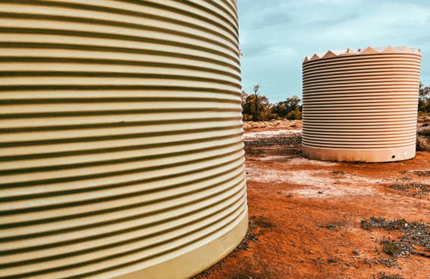 Two corrugated, cylindrical water tanks on red dirt under a blue sky. Two corrugated, cylindrical water tanks on red dirt under a blue sky.