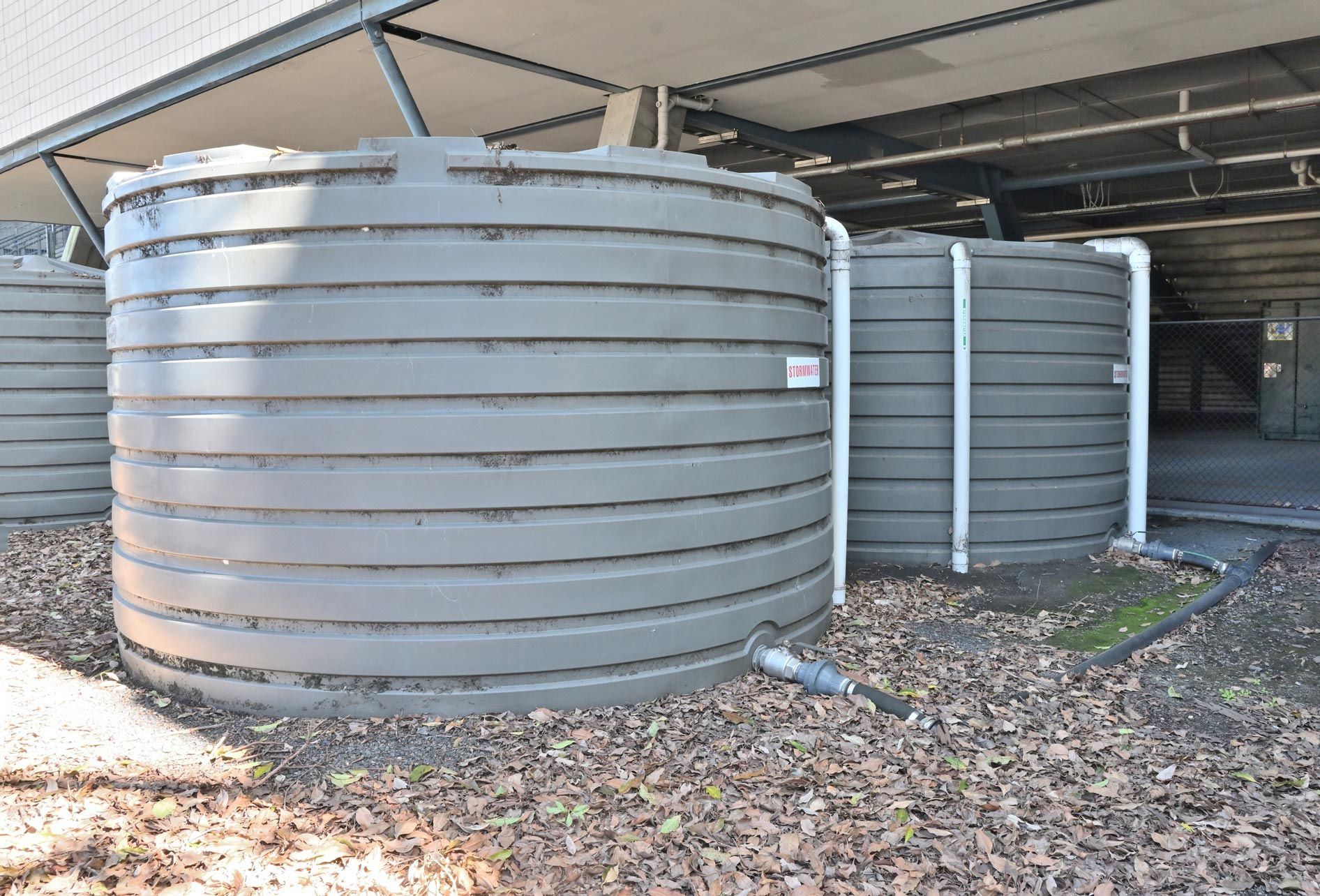 Three large, dark-gray, ribbed water tanks beneath a covered area. Three large, dark-gray, ribbed water tanks beneath a covered area.