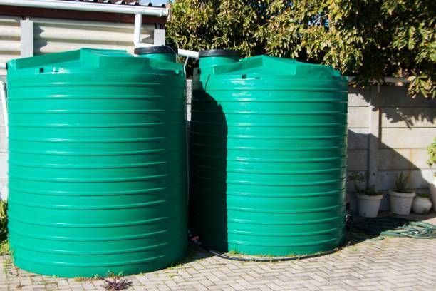 Two large, green, ribbed plastic water tanks in a backyard setting.