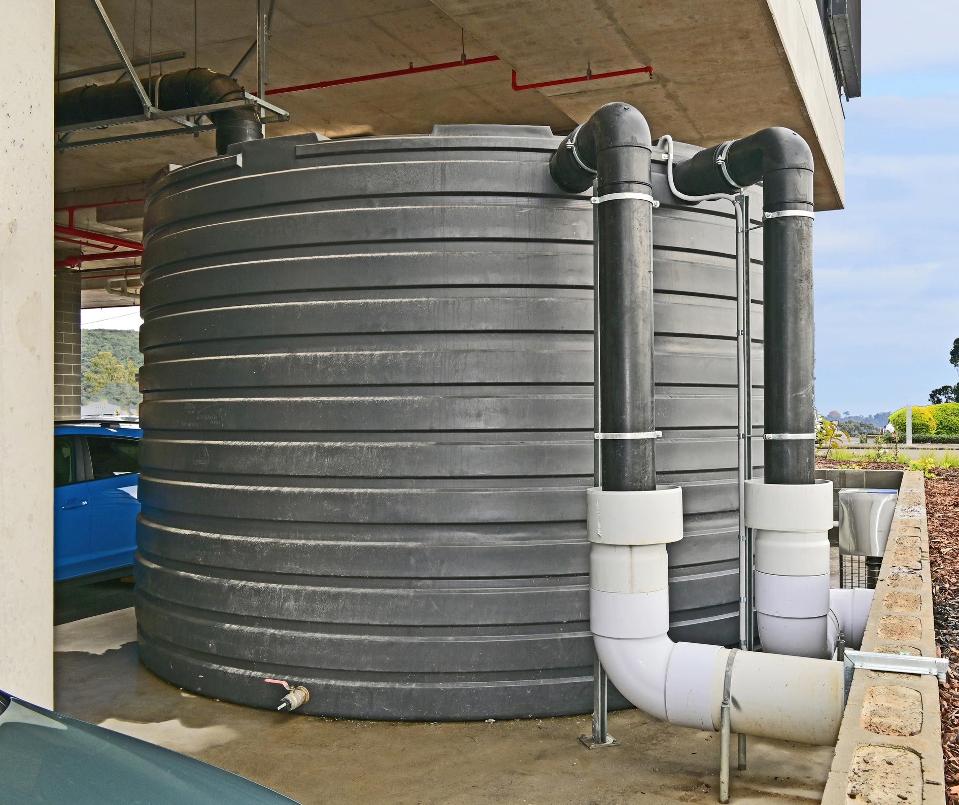 Large, black water storage tank with pipes, outdoors under a concrete structure. Large, black water storage tank with pipes, outdoors under a concrete structure.