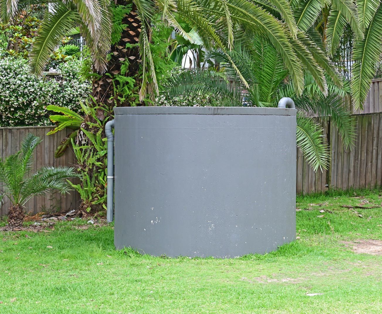 Gray circular water tank in a grassy yard, with a tree in the background. Gray circular water tank in a grassy yard, with a tree in the background.