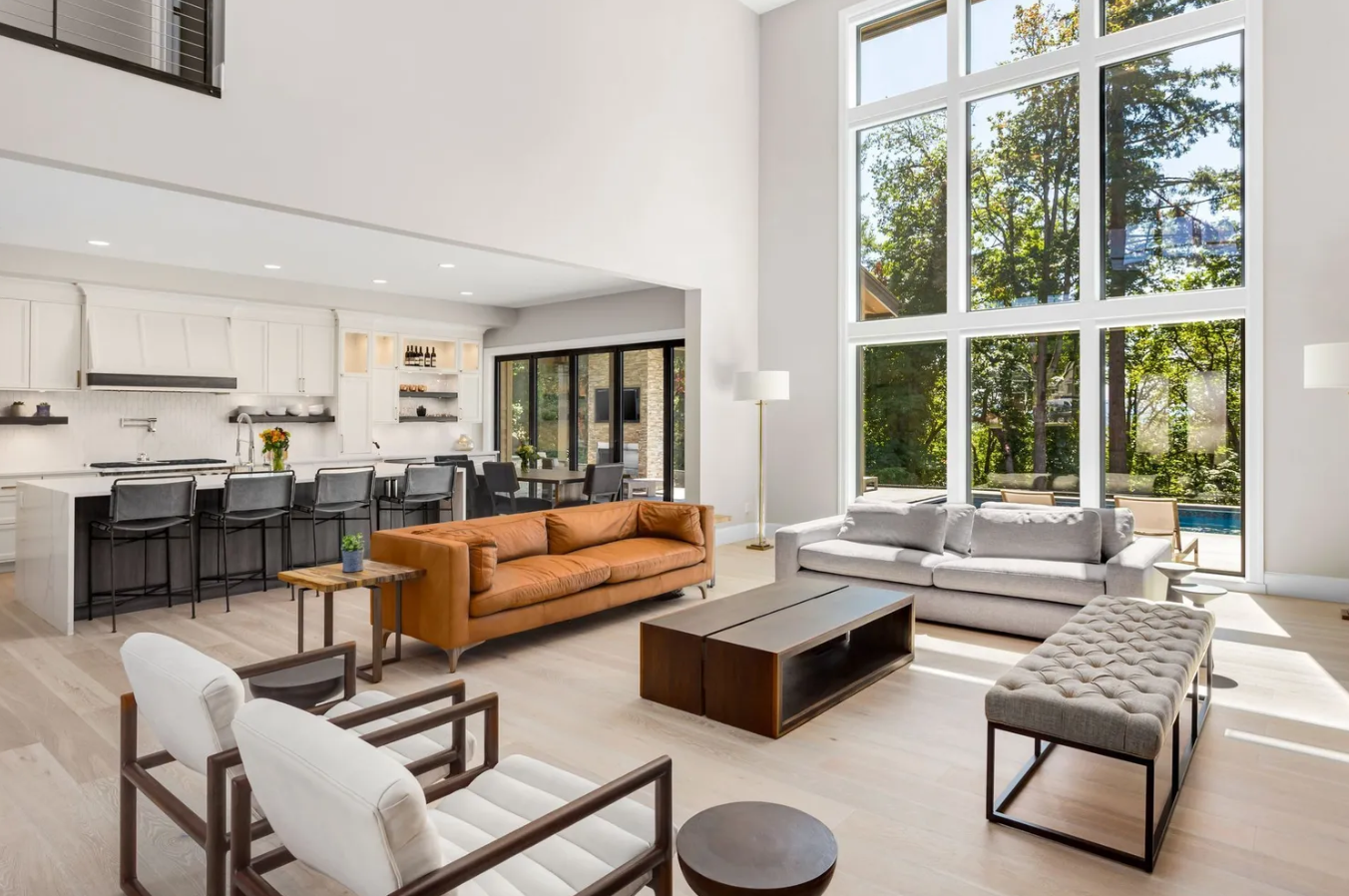 Modern living room with a kitchen, large windows, and various seating areas.