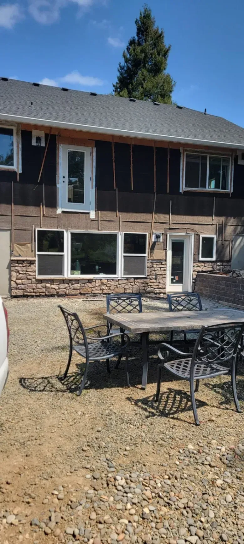Patio furniture on a gravel yard in front of a two-story brick house under a clear blue sky