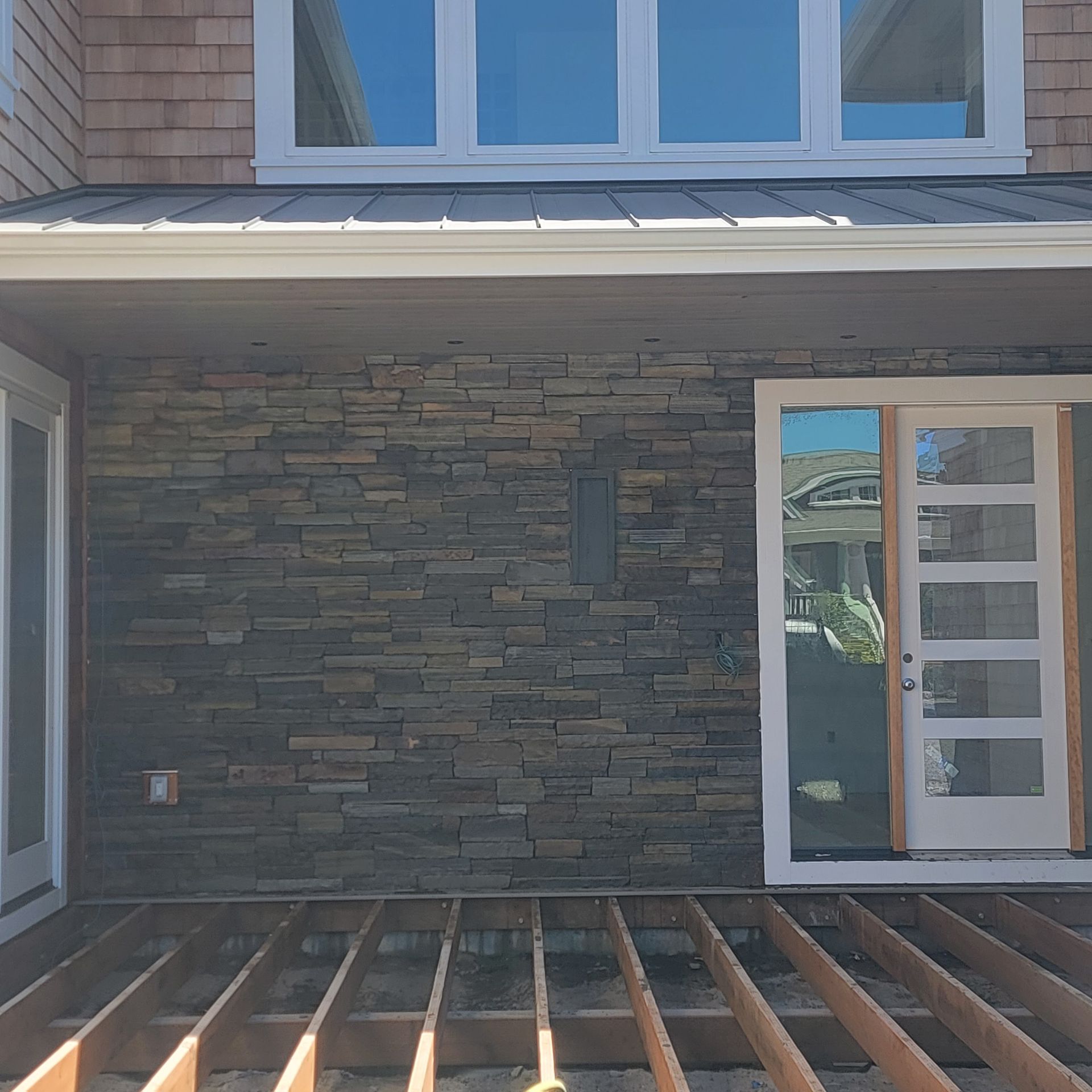Partially built wooden deck beneath a stone-clad house exterior with a sliding glass door and windows