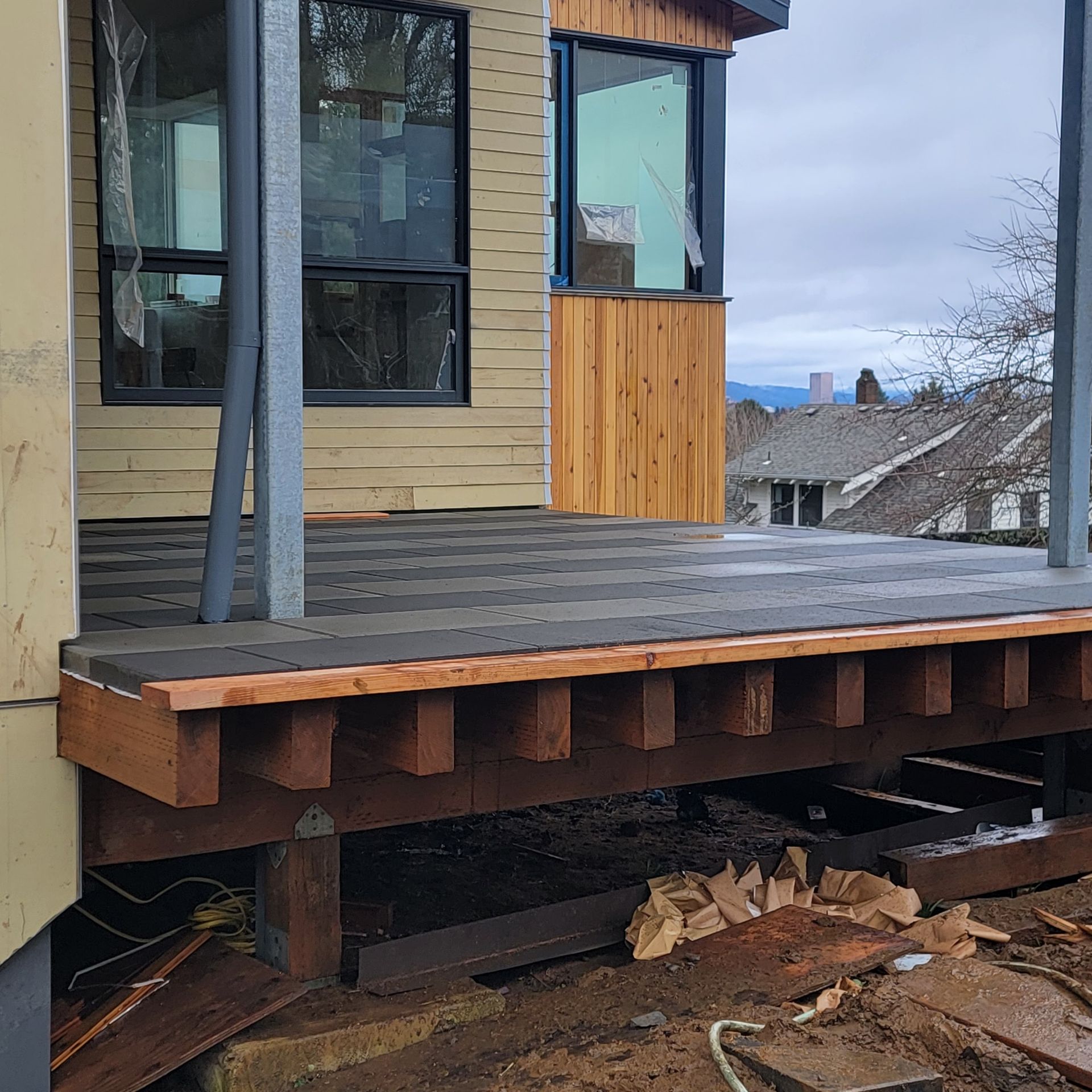 Deck under construction beside a house, with dark gray decking and exposed wooden supports.