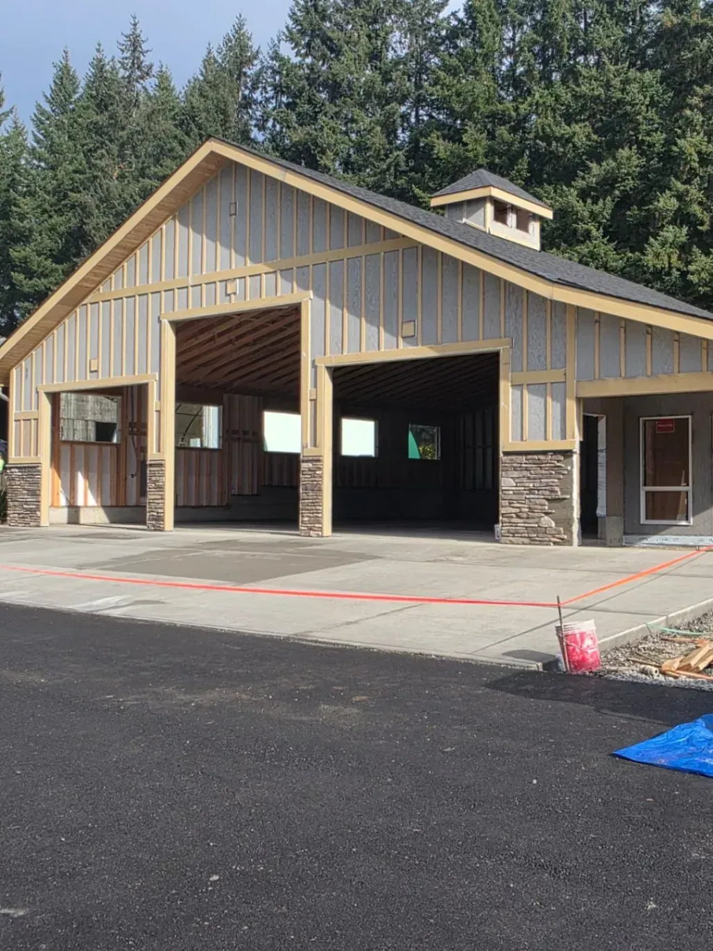 Large beige fire station with open garage bays and stone accents beside a paved lot and trees.