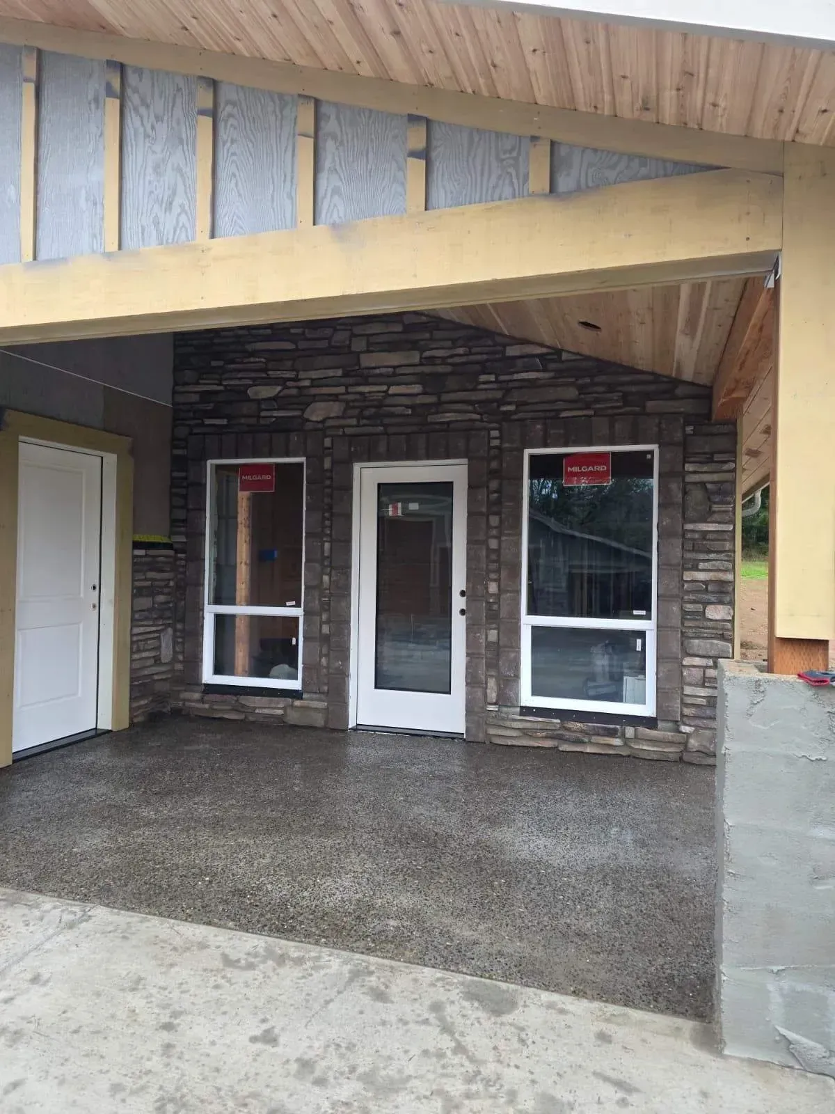 Covered storefront with three front doors, brick wall, and wet concrete walkway under a wooden awning