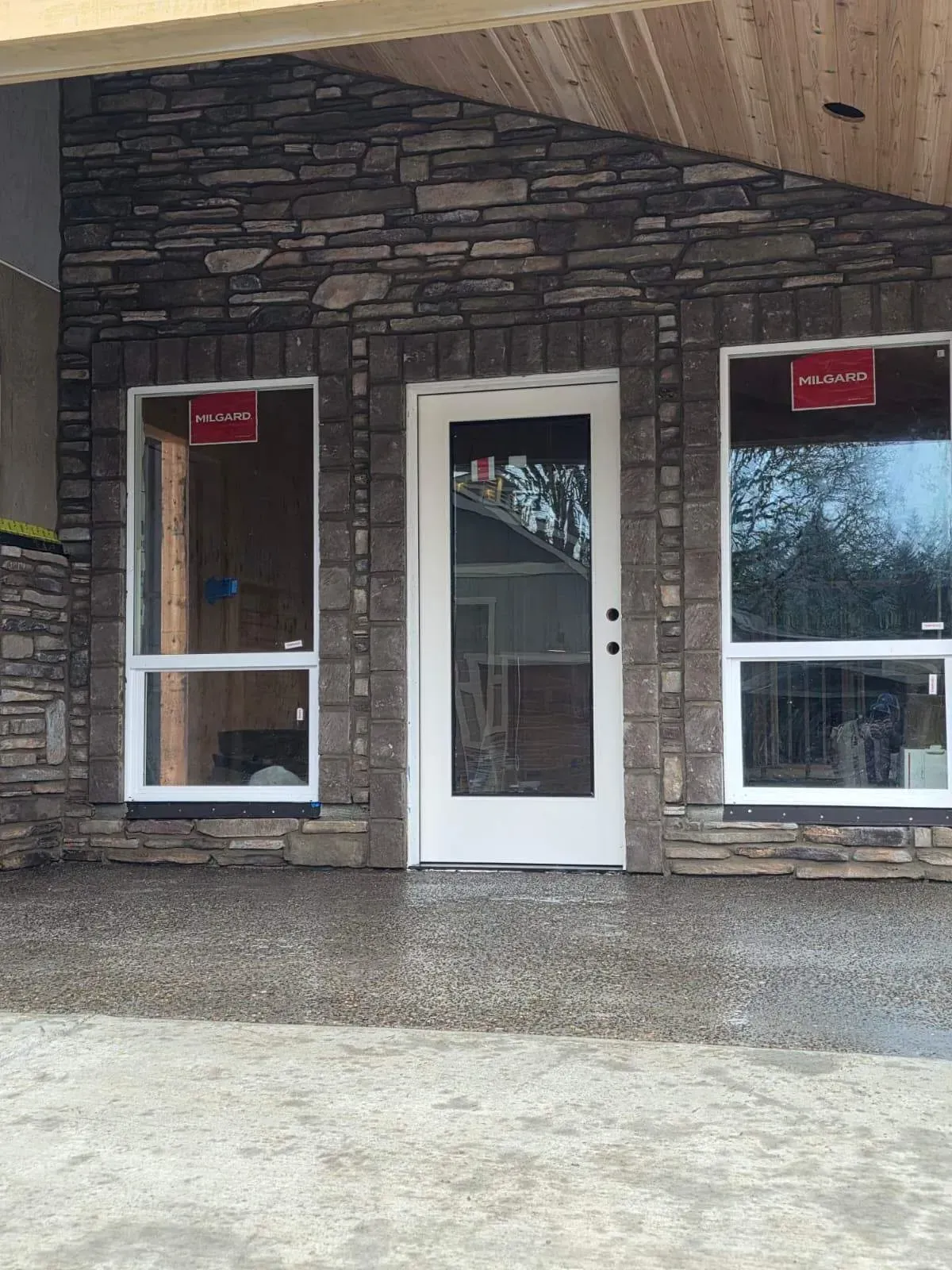 Stone-front storefront with a white door and two windows, each displaying a red sign.