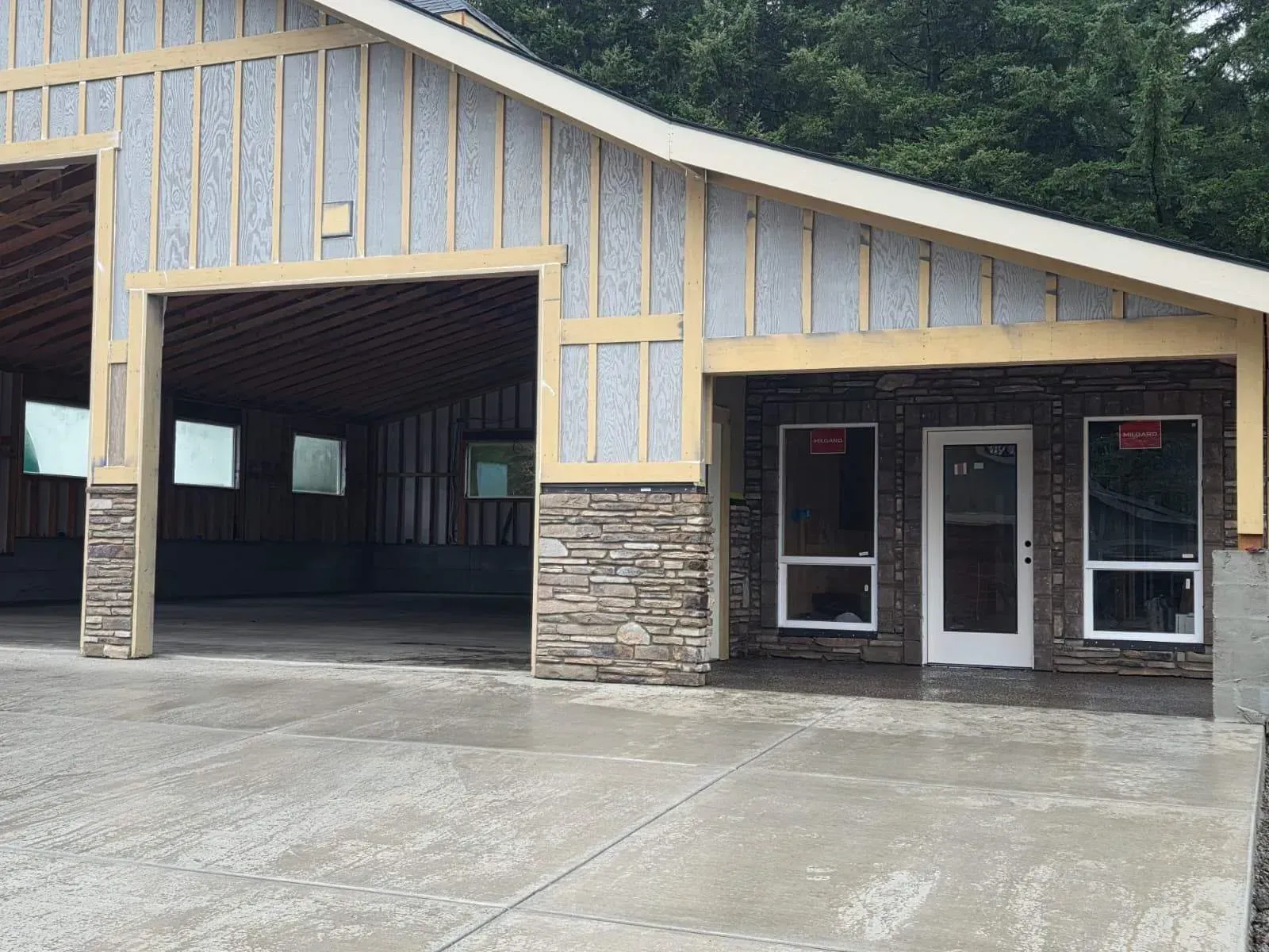 Front view of a small building with a curved roof, stone columns, and a large open garage bay.