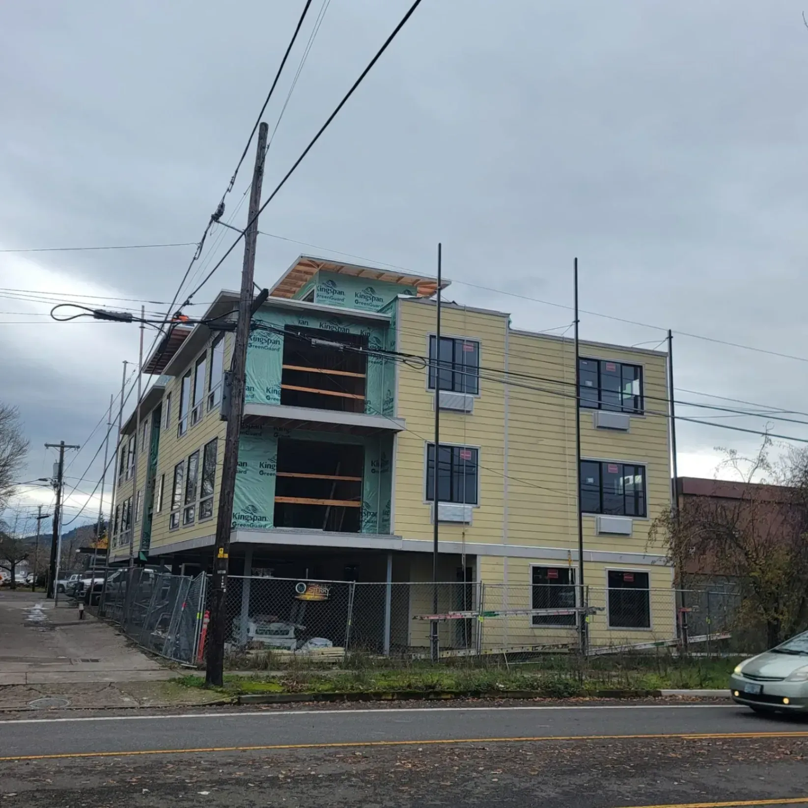 Three-story apartment building under construction on a street corner, with scaffolding and utility poles.