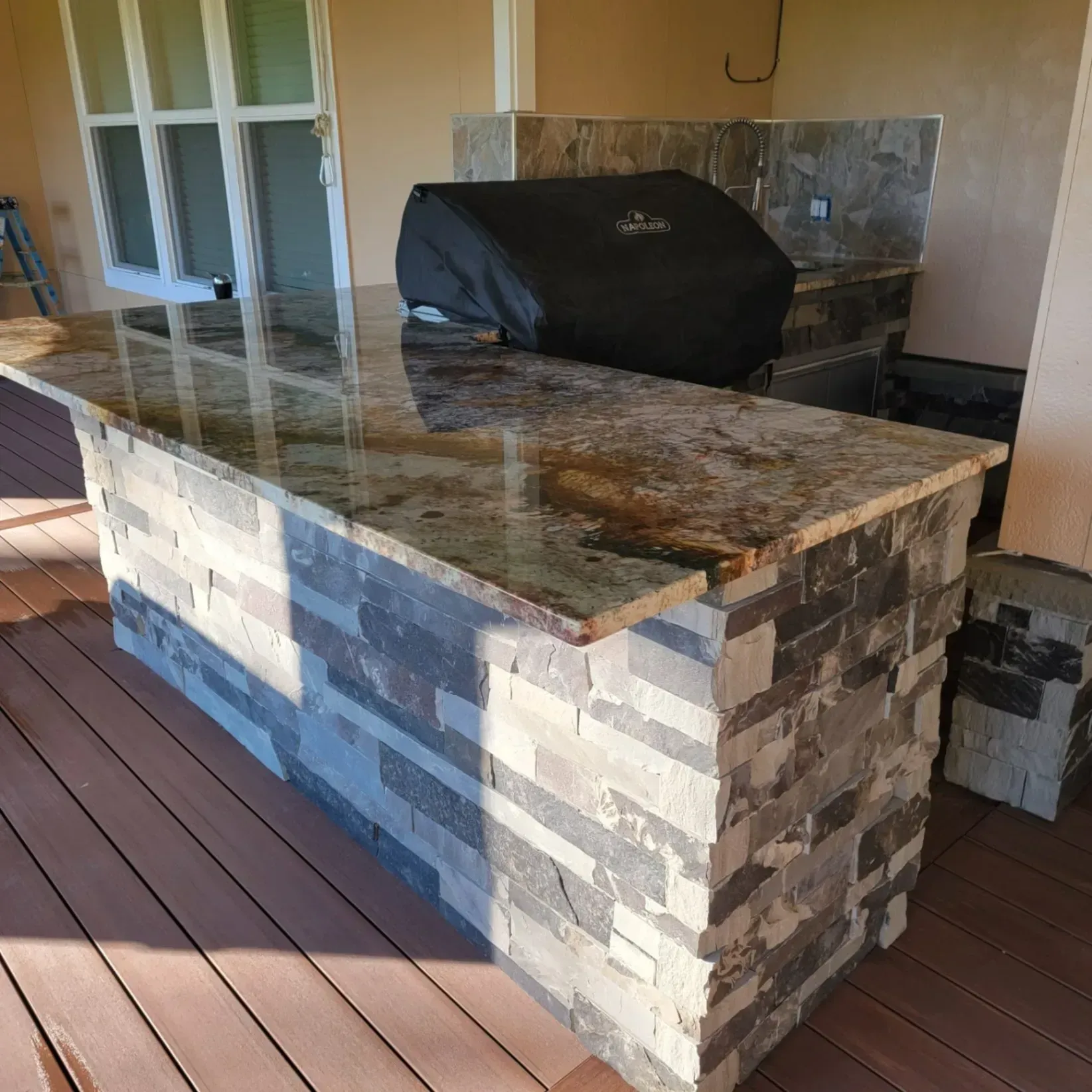 Outdoor patio with stone-tiled countertop and built-in grill beside a wooden deck and sliding glass doors